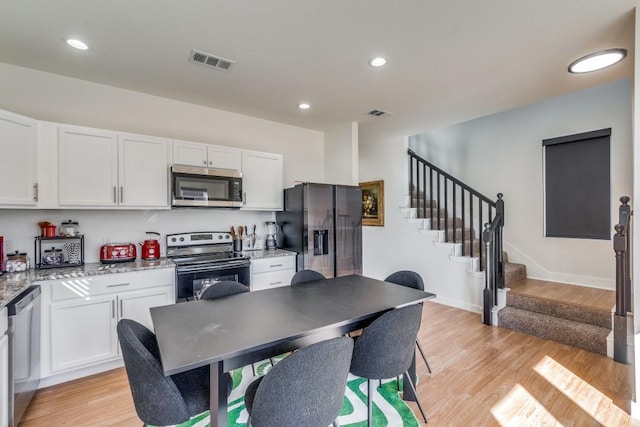 kitchen with white cabinetry, light wood-type flooring, light stone countertops, and appliances with stainless steel finishes