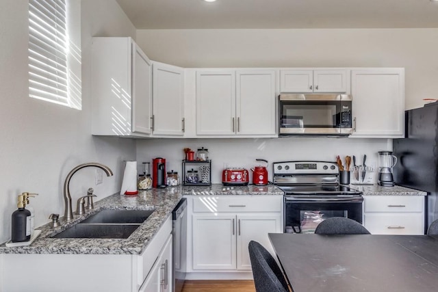 kitchen featuring sink, stone counters, white cabinetry, appliances with stainless steel finishes, and light hardwood / wood-style floors