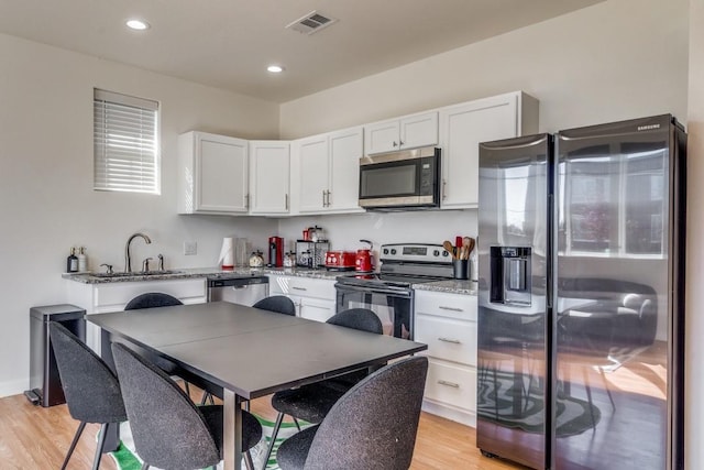 kitchen with sink, white cabinetry, light stone counters, light wood-type flooring, and stainless steel appliances