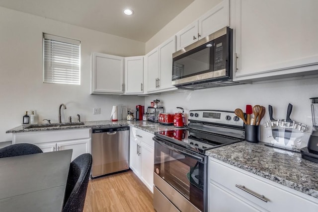 kitchen featuring sink, light hardwood / wood-style flooring, stone counters, appliances with stainless steel finishes, and white cabinets