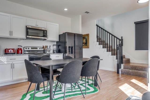 kitchen with stainless steel appliances, white cabinetry, light stone counters, and light wood-type flooring