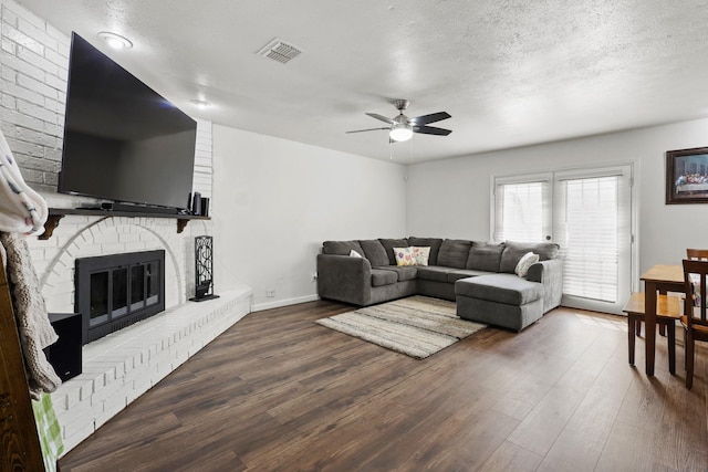 living room with ceiling fan, wood-type flooring, a brick fireplace, and a textured ceiling