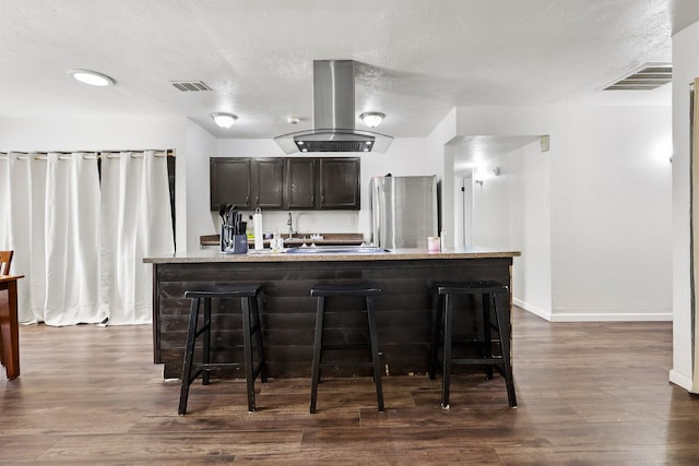 kitchen featuring a center island with sink, stainless steel fridge, a kitchen breakfast bar, dark hardwood / wood-style flooring, and island exhaust hood