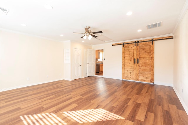 unfurnished bedroom featuring hardwood / wood-style flooring, crown molding, a barn door, and ceiling fan