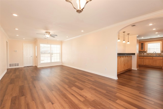 unfurnished living room featuring sink, crown molding, dark wood-type flooring, and ceiling fan