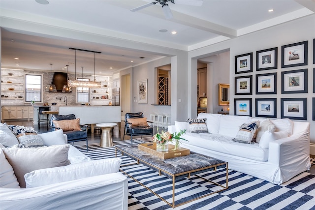 living room with sink, crown molding, beamed ceiling, and ceiling fan