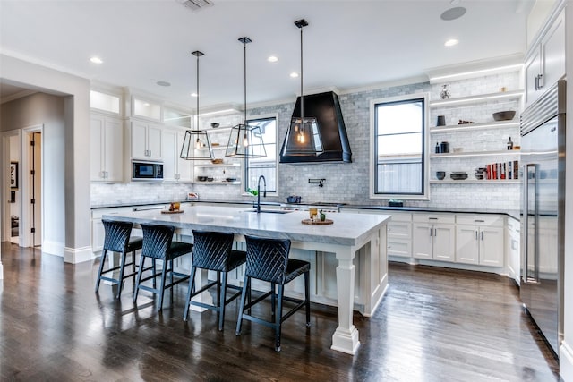 kitchen with a center island with sink, built in appliances, custom exhaust hood, and white cabinets