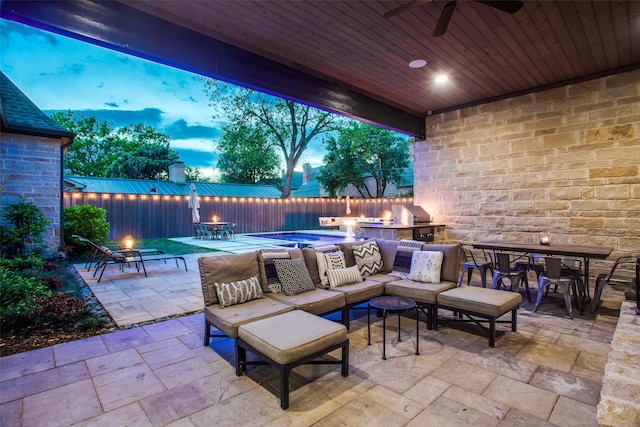 patio terrace at dusk with an outdoor living space with a fire pit, ceiling fan, and exterior kitchen