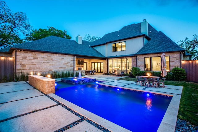 pool at dusk with pool water feature, an in ground hot tub, and a patio