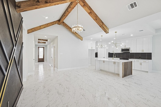 kitchen with pendant lighting, tasteful backsplash, a notable chandelier, an island with sink, and white cabinets