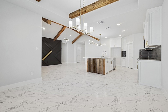 kitchen featuring pendant lighting, beamed ceiling, an island with sink, sink, and white cabinets