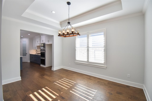 unfurnished dining area featuring dark wood-type flooring, ornamental molding, a tray ceiling, and a notable chandelier