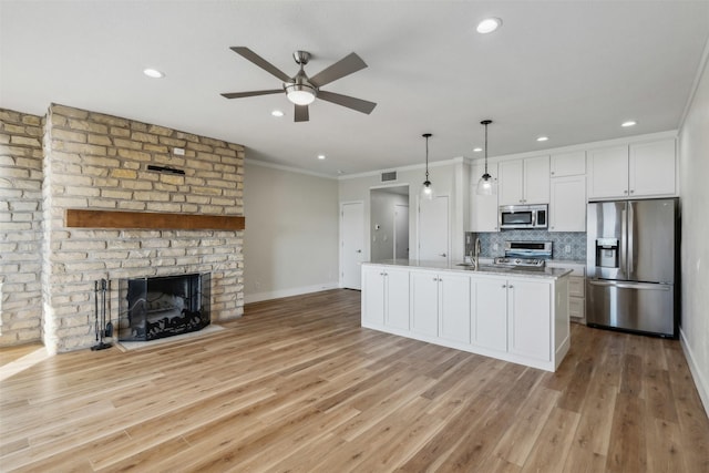 kitchen with pendant lighting, stainless steel appliances, light stone countertops, an island with sink, and white cabinets