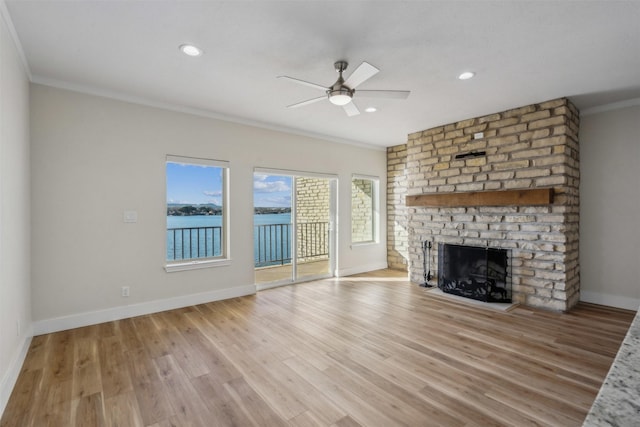 unfurnished living room featuring crown molding, a water view, a fireplace, and light hardwood / wood-style floors