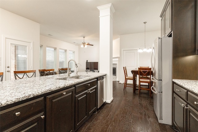 kitchen featuring sink, hanging light fixtures, stainless steel appliances, light stone countertops, and dark wood-type flooring