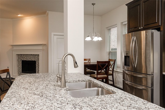 kitchen with sink, an inviting chandelier, stainless steel fridge, a tile fireplace, and light stone countertops