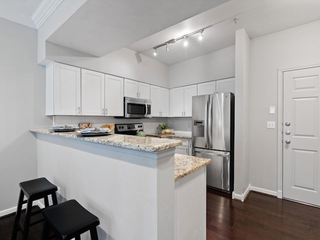 kitchen with appliances with stainless steel finishes, kitchen peninsula, white cabinets, light stone countertops, and backsplash