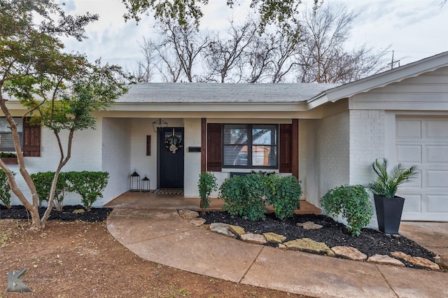 doorway to property with a garage, brick siding, and a shingled roof