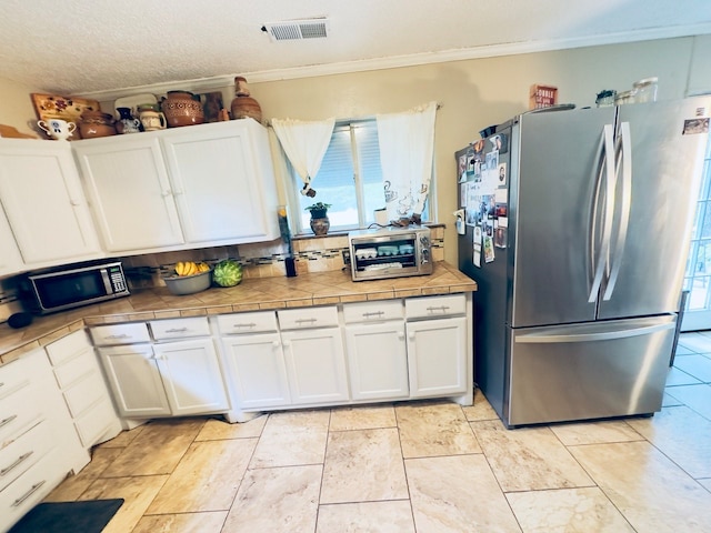 kitchen with light tile patterned floors, white cabinetry, stainless steel appliances, decorative backsplash, and tile countertops