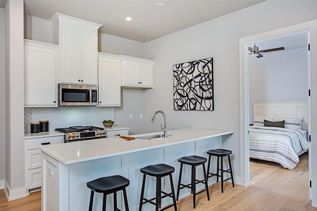 kitchen with sink, light hardwood / wood-style flooring, a breakfast bar, white cabinetry, and stainless steel appliances