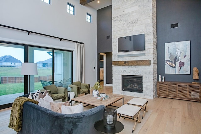 living room with a stone fireplace, light hardwood / wood-style floors, and a high ceiling