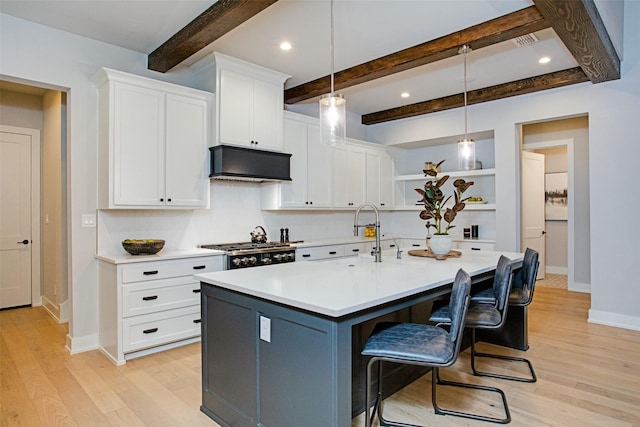 kitchen with a kitchen bar, decorative light fixtures, ventilation hood, a center island with sink, and white cabinets