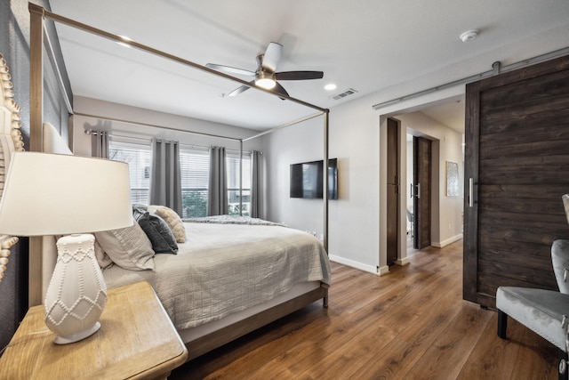 bedroom featuring dark hardwood / wood-style flooring, a barn door, and ceiling fan