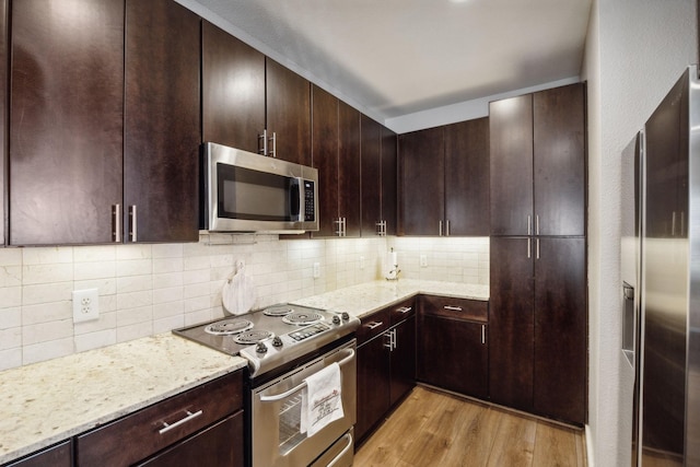 kitchen with light stone counters, dark brown cabinets, stainless steel appliances, light hardwood / wood-style floors, and decorative backsplash