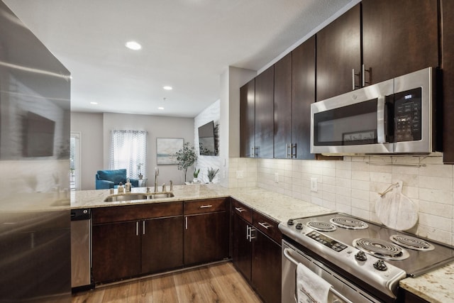 kitchen with sink, light hardwood / wood-style flooring, appliances with stainless steel finishes, light stone countertops, and kitchen peninsula