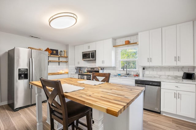 kitchen with tasteful backsplash, sink, white cabinets, light hardwood / wood-style floors, and stainless steel appliances