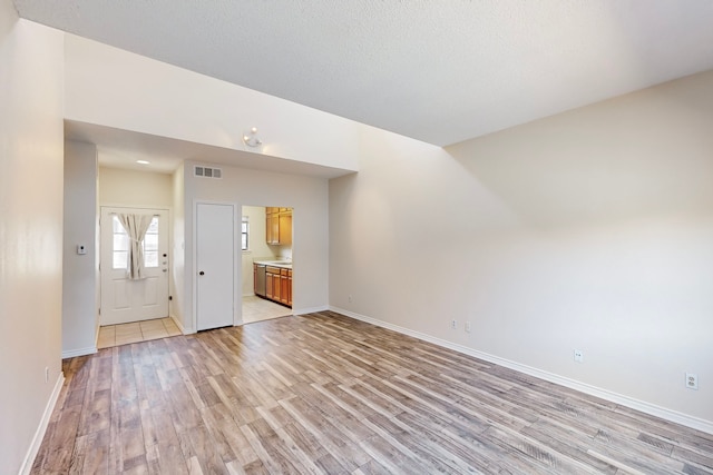 unfurnished living room with lofted ceiling, a textured ceiling, and light wood-type flooring