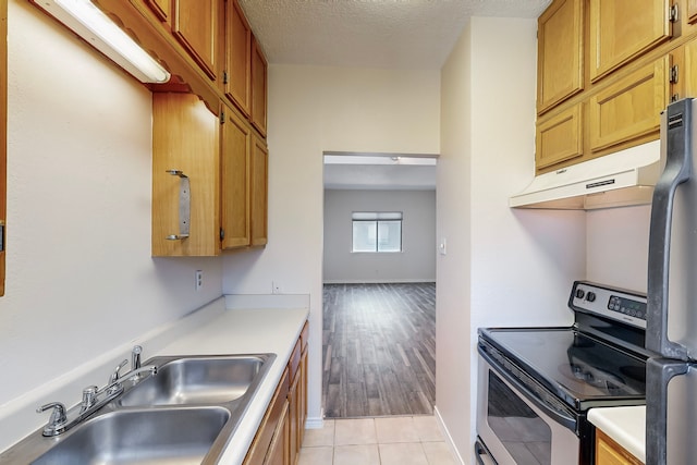 kitchen featuring electric range, a sink, a textured ceiling, freestanding refrigerator, and light countertops