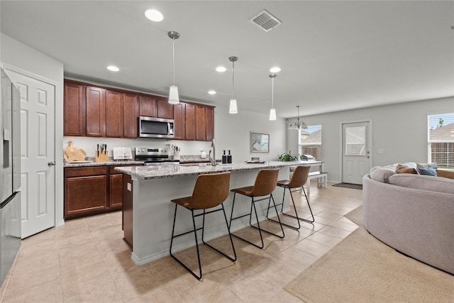 kitchen featuring appliances with stainless steel finishes, pendant lighting, a kitchen breakfast bar, light stone countertops, and a center island with sink