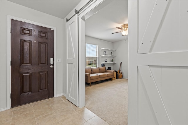 foyer featuring a barn door, light colored carpet, and ceiling fan