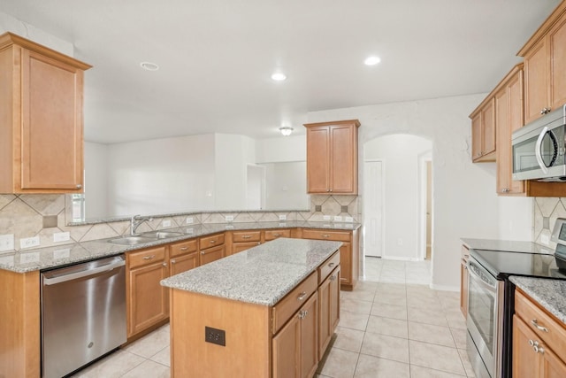 kitchen with sink, a kitchen island, stainless steel appliances, light stone countertops, and light tile patterned flooring