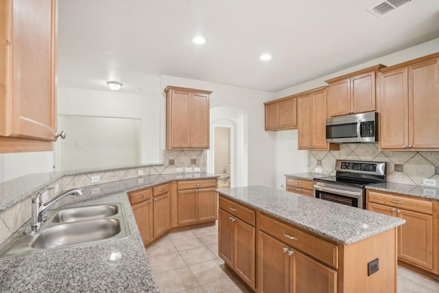 kitchen featuring sink, appliances with stainless steel finishes, light stone counters, tasteful backsplash, and a kitchen island