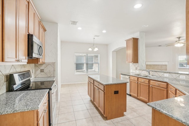 kitchen featuring sink, decorative light fixtures, a center island, stainless steel appliances, and light stone countertops