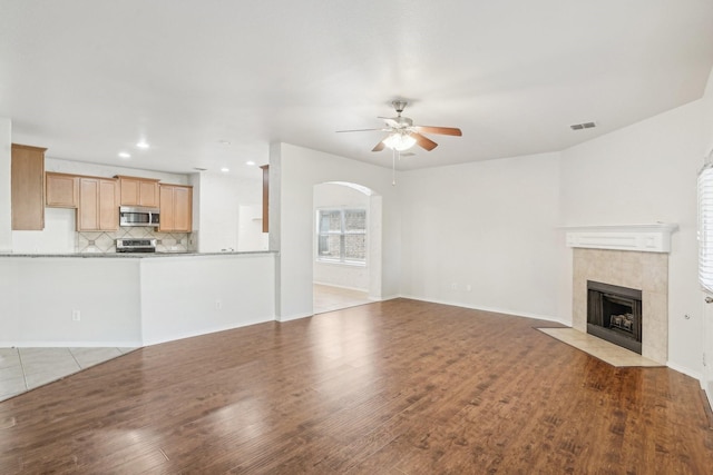 unfurnished living room with a tiled fireplace, light hardwood / wood-style flooring, and ceiling fan