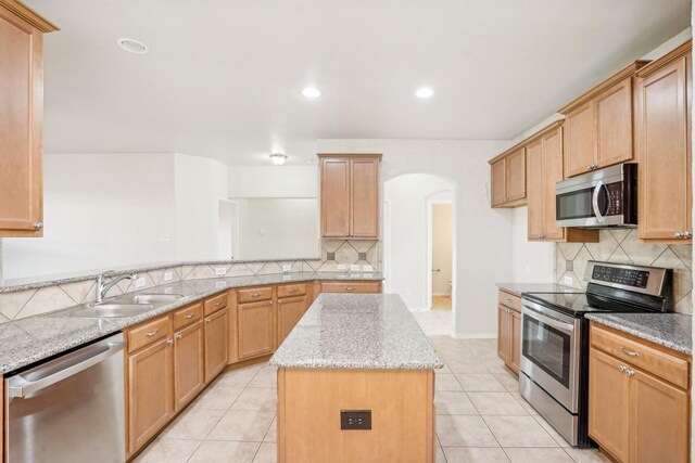 kitchen with light tile patterned flooring, sink, a center island, stainless steel appliances, and light stone countertops