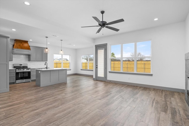 kitchen with gray cabinets, stainless steel electric range oven, decorative light fixtures, a kitchen island with sink, and custom range hood