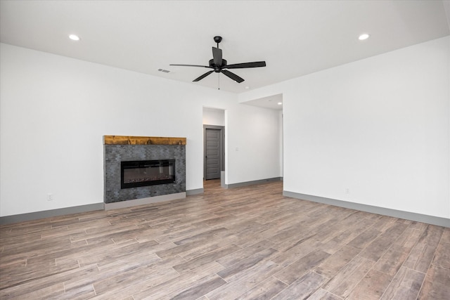 unfurnished living room featuring a tiled fireplace, ceiling fan, and light hardwood / wood-style flooring