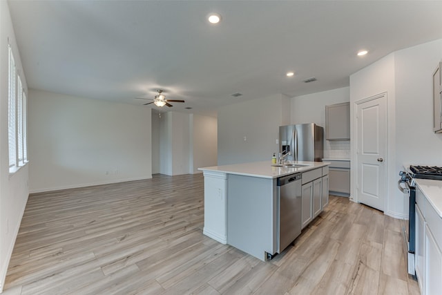 kitchen with gray cabinets, an island with sink, stainless steel appliances, and light wood-type flooring