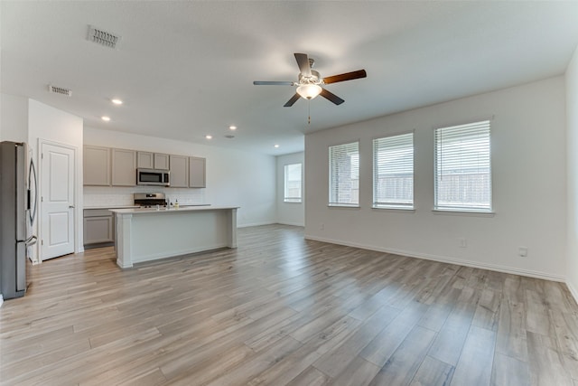 kitchen featuring appliances with stainless steel finishes, backsplash, light hardwood / wood-style floors, gray cabinets, and an island with sink