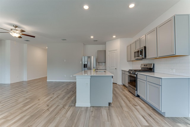 kitchen with an island with sink, gray cabinetry, light hardwood / wood-style flooring, appliances with stainless steel finishes, and decorative backsplash