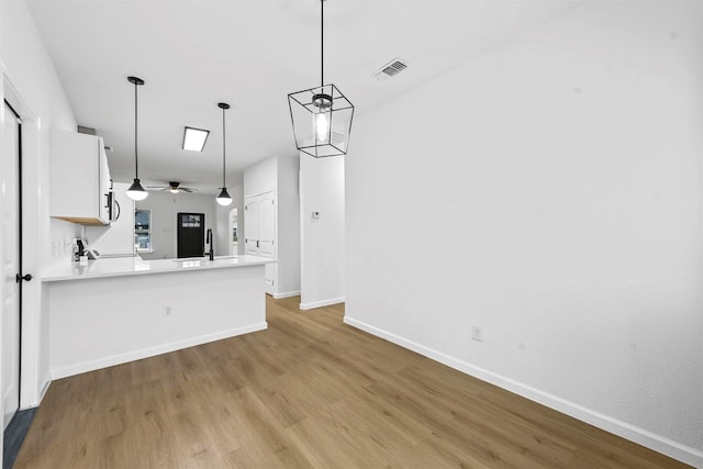 kitchen with decorative light fixtures, kitchen peninsula, ceiling fan, light hardwood / wood-style floors, and white cabinets