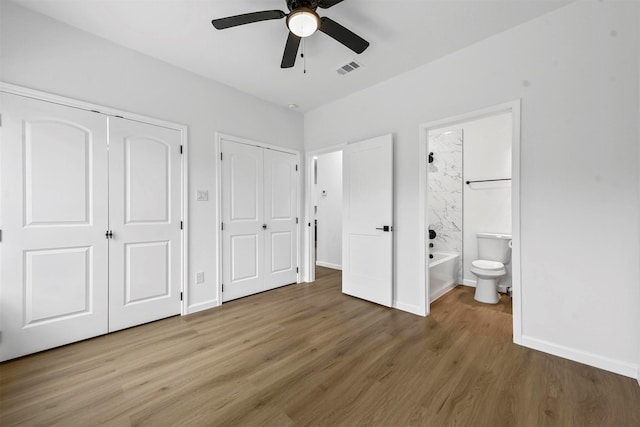 unfurnished bedroom with hardwood / wood-style floors, ceiling fan, multiple closets, and ensuite bathroom