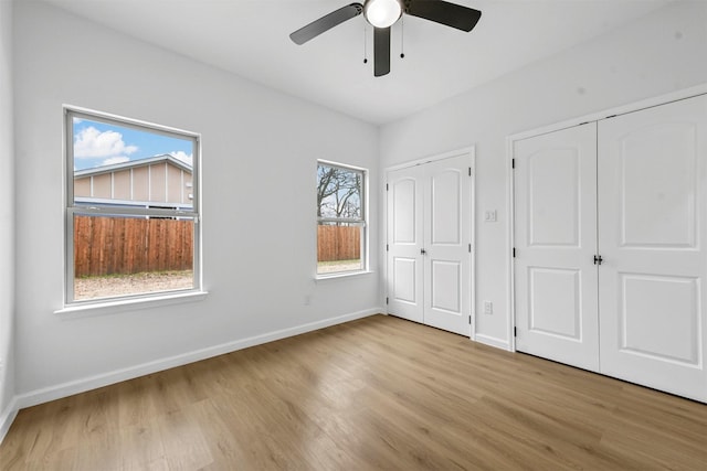 unfurnished bedroom featuring ceiling fan, light wood-type flooring, and two closets