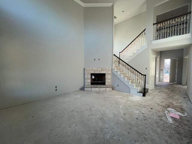 unfurnished living room with stairs, a high ceiling, a fireplace, and crown molding