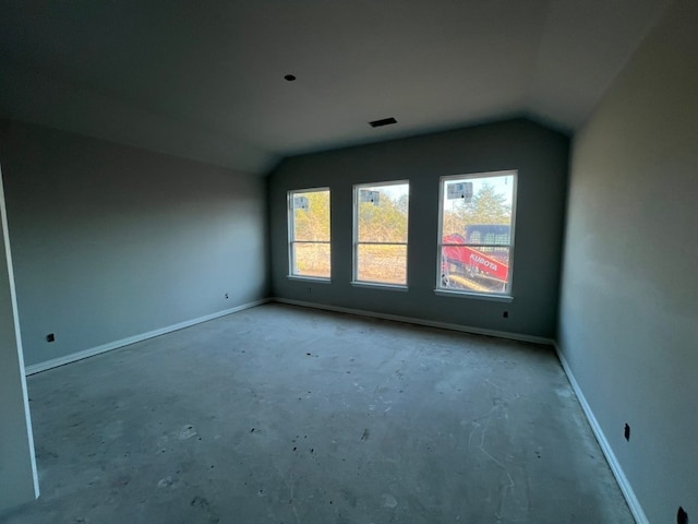 empty room with concrete flooring, lofted ceiling, visible vents, and baseboards