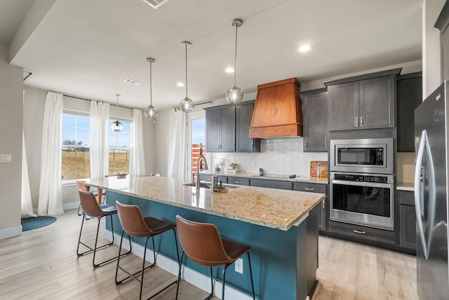 kitchen with light stone counters, appliances with stainless steel finishes, tasteful backsplash, a kitchen bar, and custom range hood